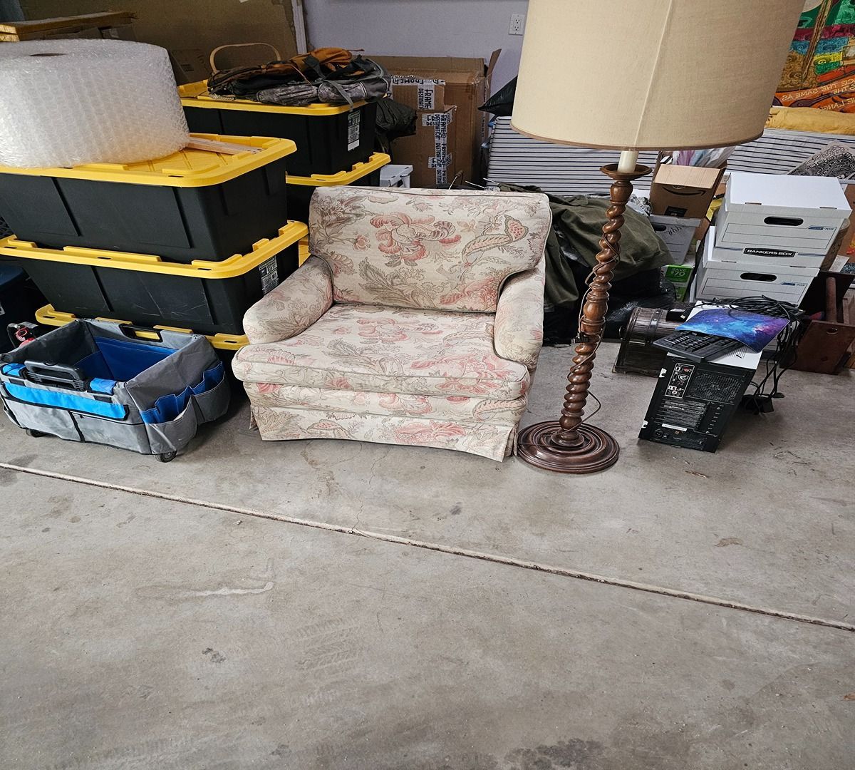 Floral armchair and floor lamp in a cluttered garage with storage bins and boxes