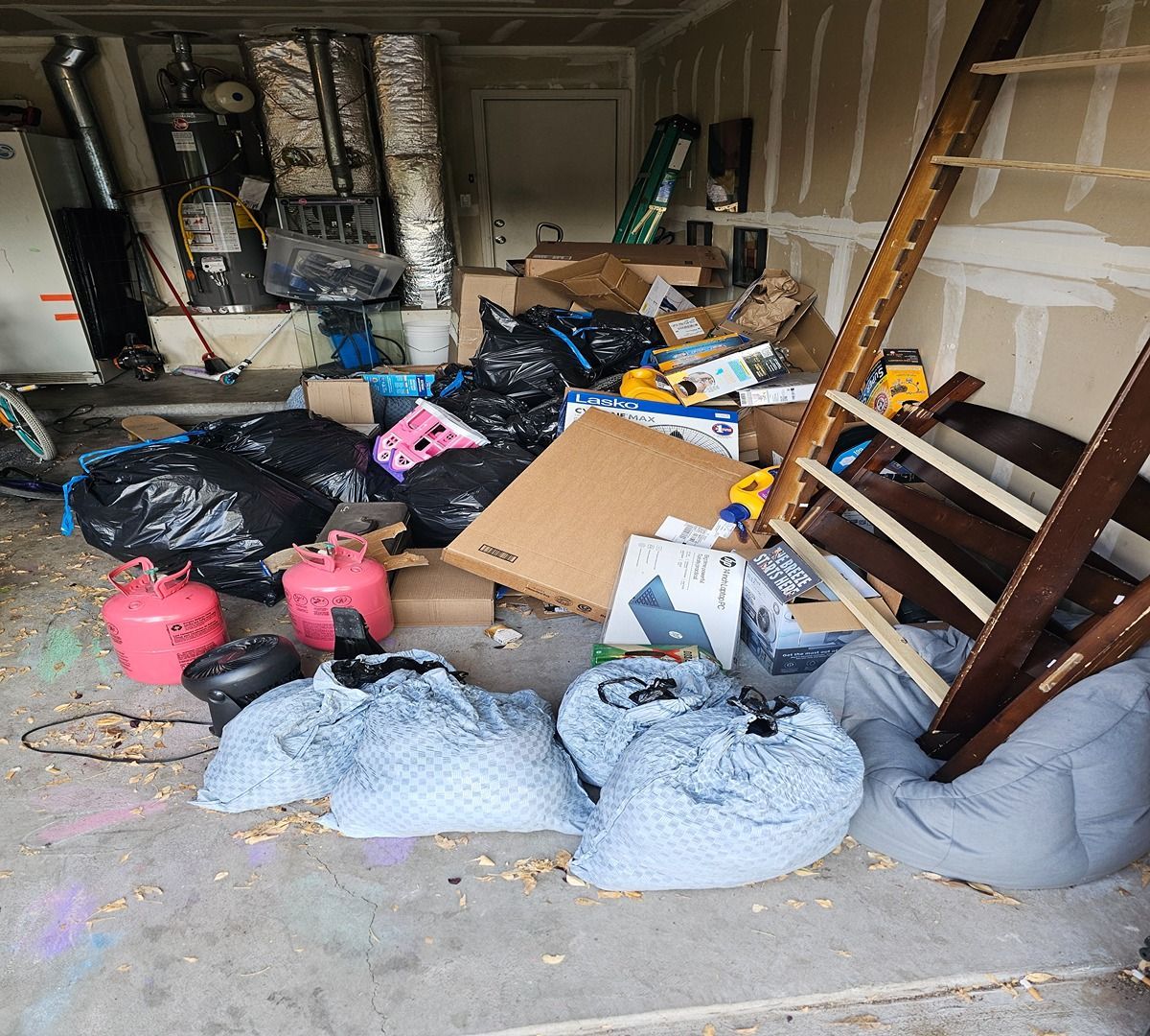 Cluttered garage with trash bags, boxes, and debris piled across the floor.