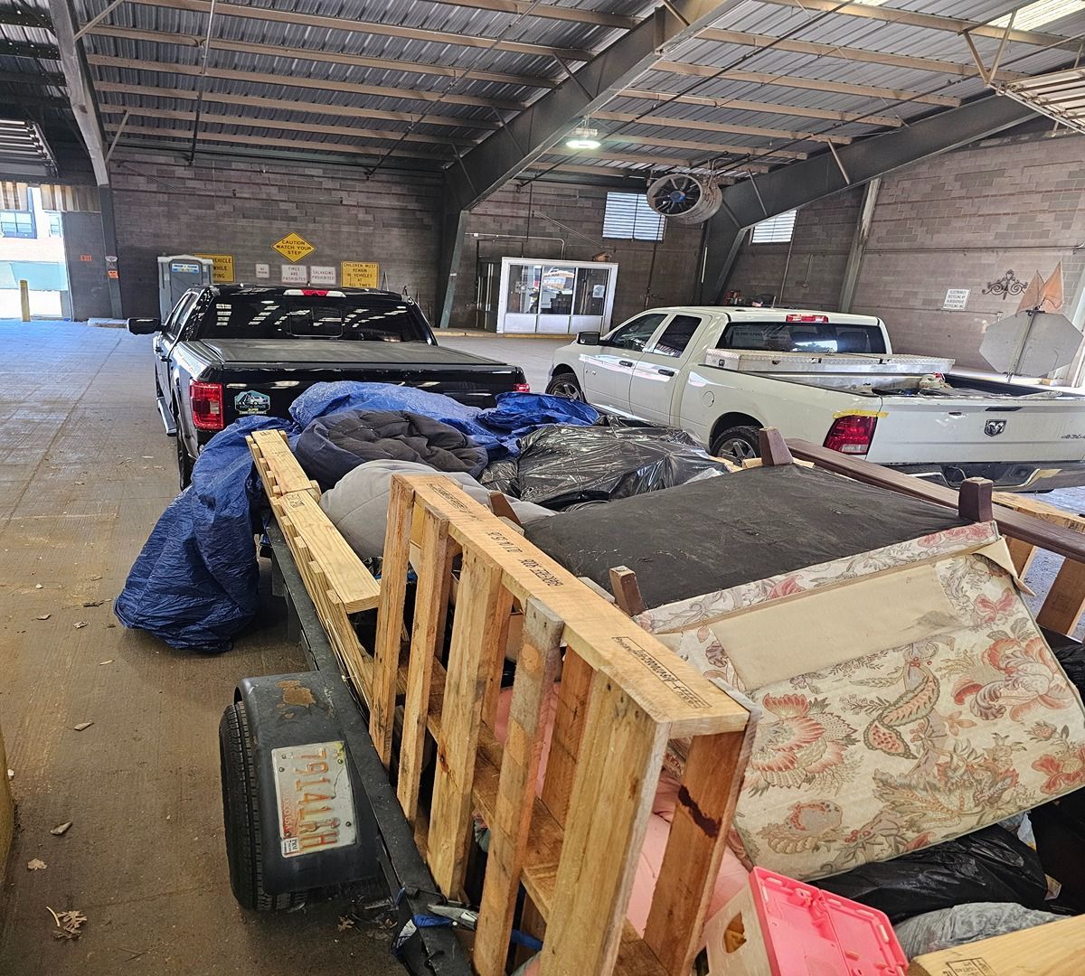 Indoor warehouse with several pickup trucks and a trailer loaded with furniture and tarps.