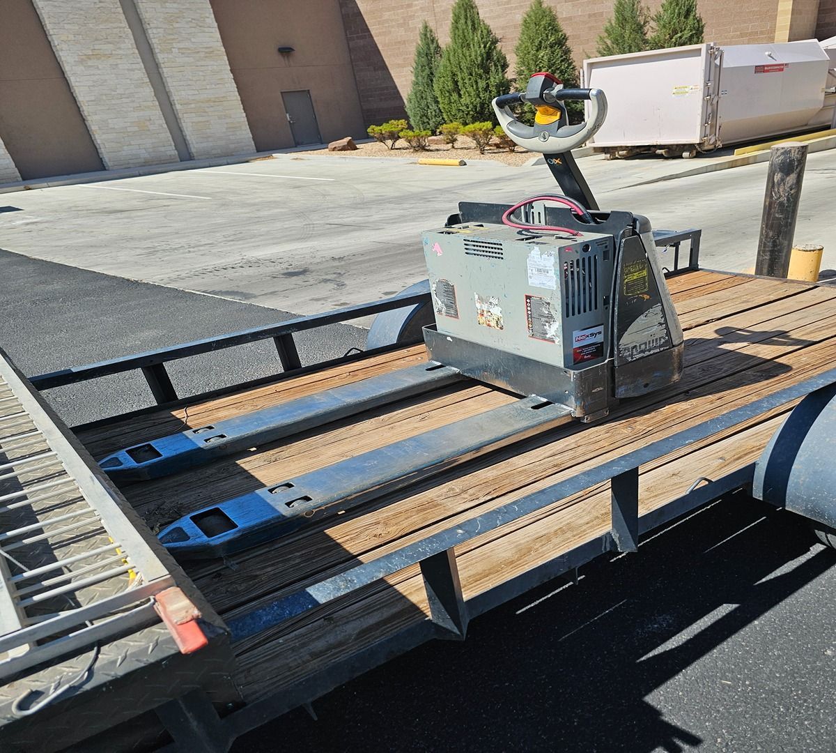 Small robot on a flatbed trailer in a parking lot, with boxes and pallets nearby.