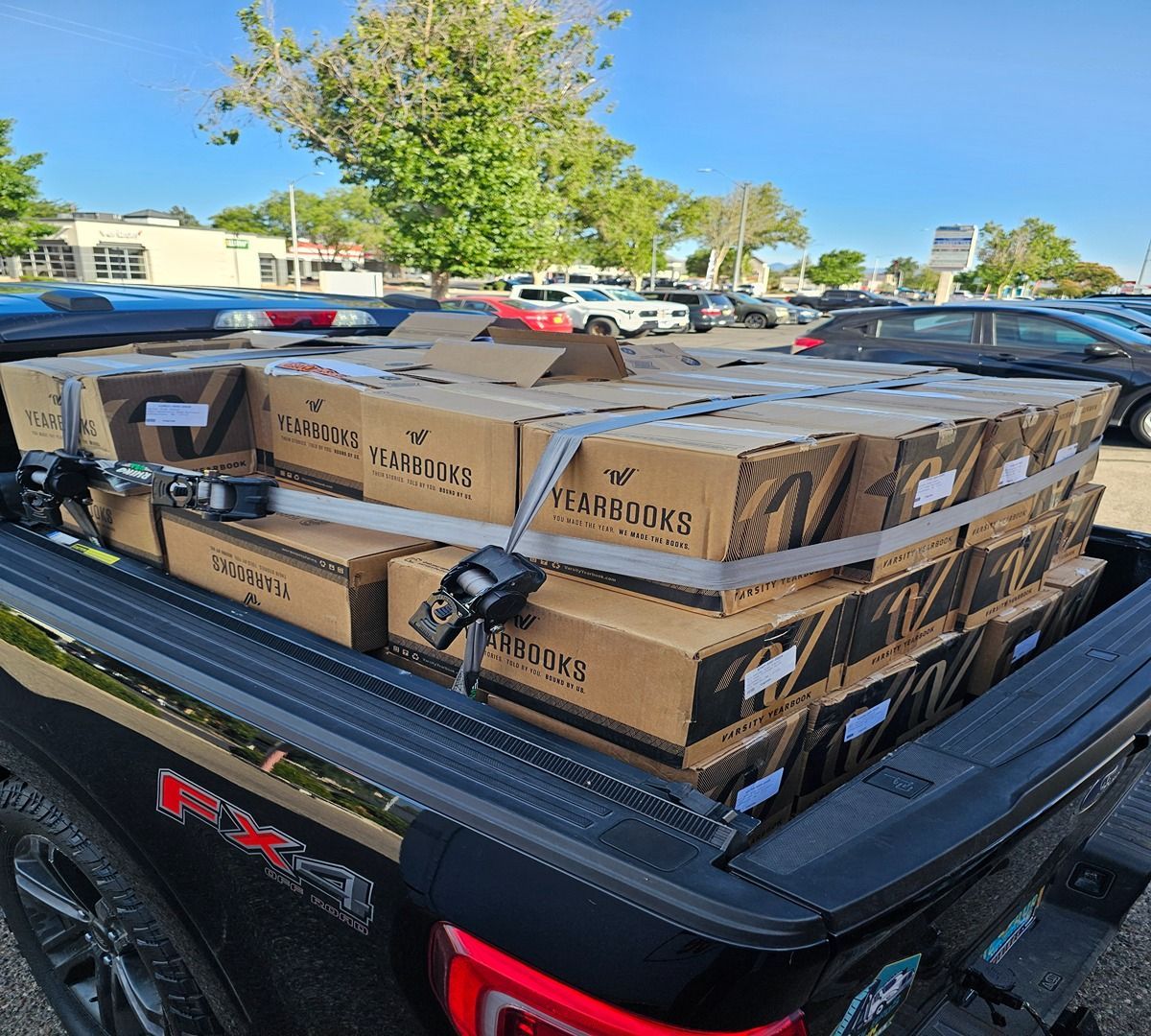 Pickup truck bed loaded with stacked cardboard boxes and a strapped-down cargo rack in a parking lot