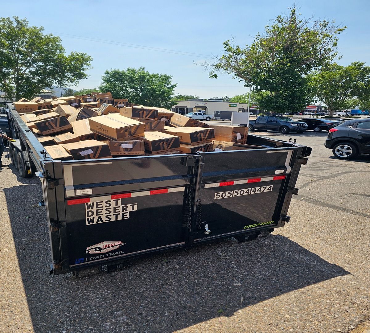 Black dumpster filled with broken wooden pallets in a parking lot on a sunny day