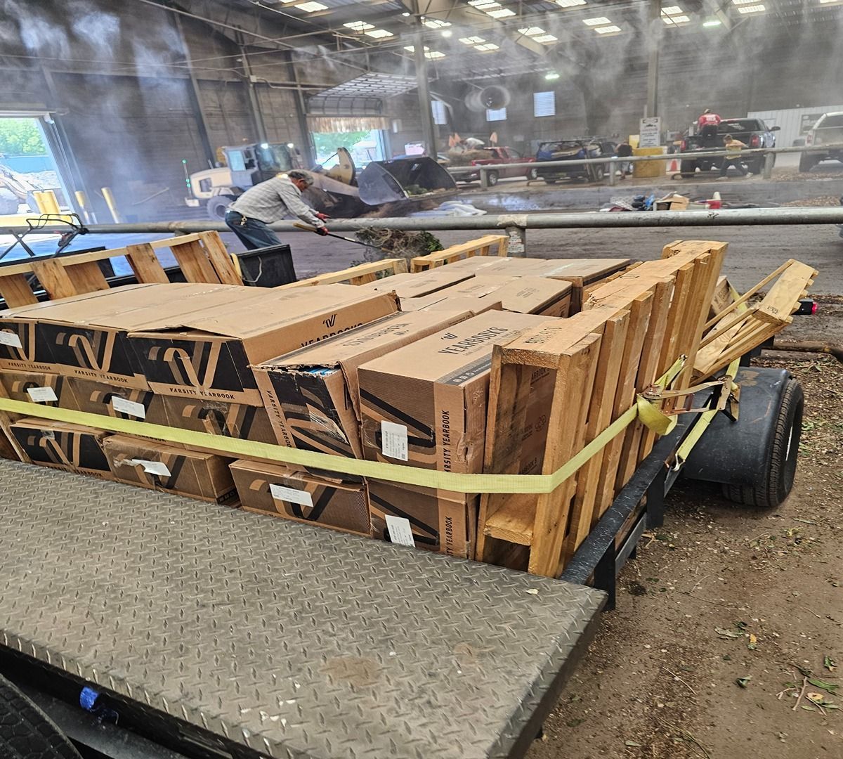 Trailer loaded with bundled wood pallets secured by a yellow strap in a warehouse setting