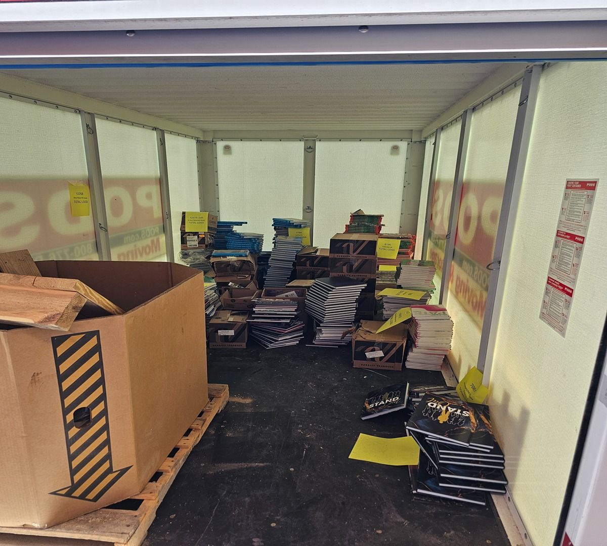 Storage container filled with stacked books, boxes, and scattered papers on the floor