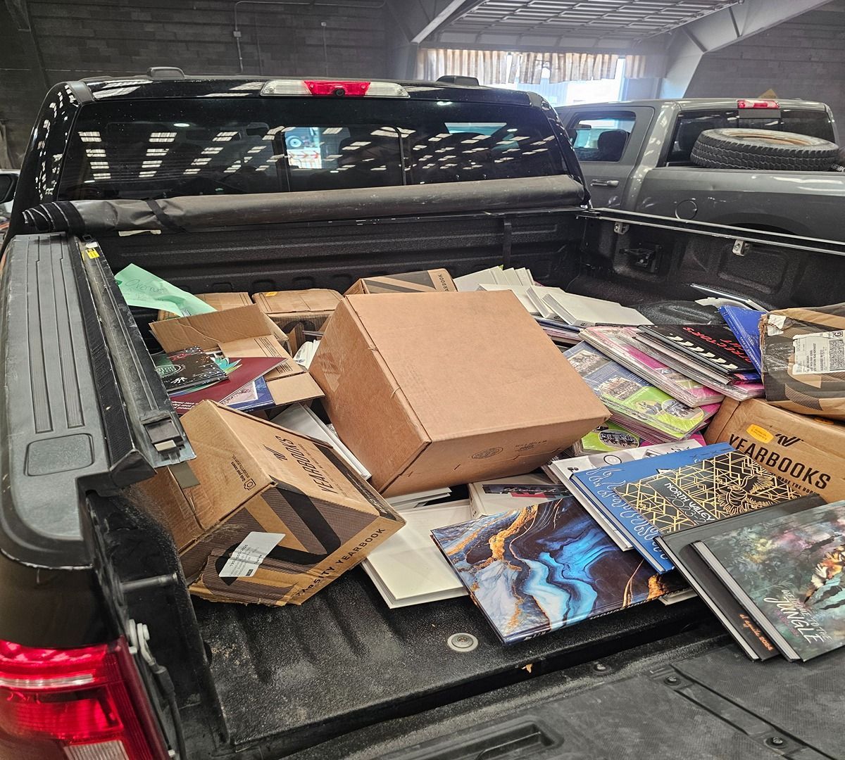 Pickup truck bed filled with cardboard boxes, books, and magazines in a garage or warehouse.