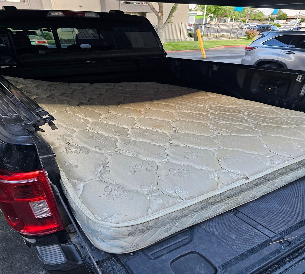 Mattress in the bed of a black pickup truck, with a parking lot visible behind it.
