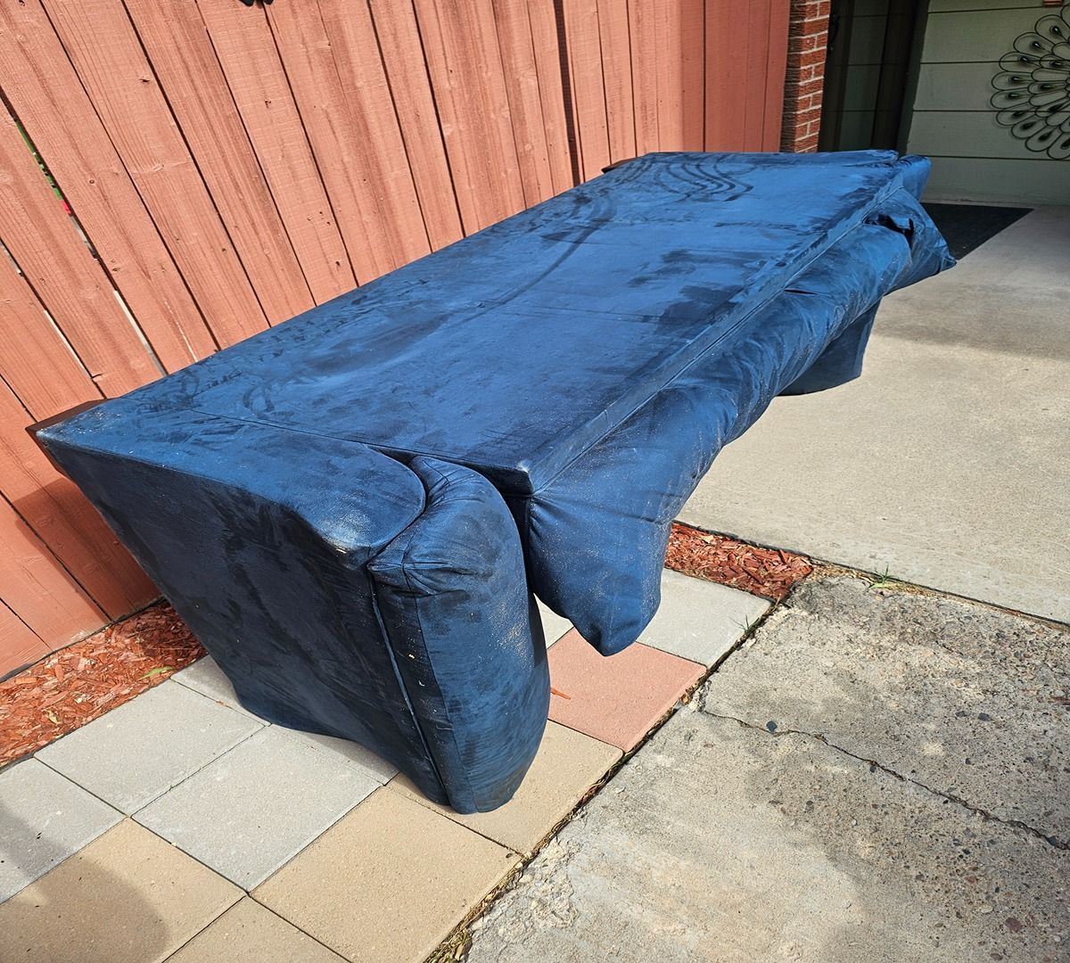 Blue-covered outdoor bench against a wooden fence on a paved patio