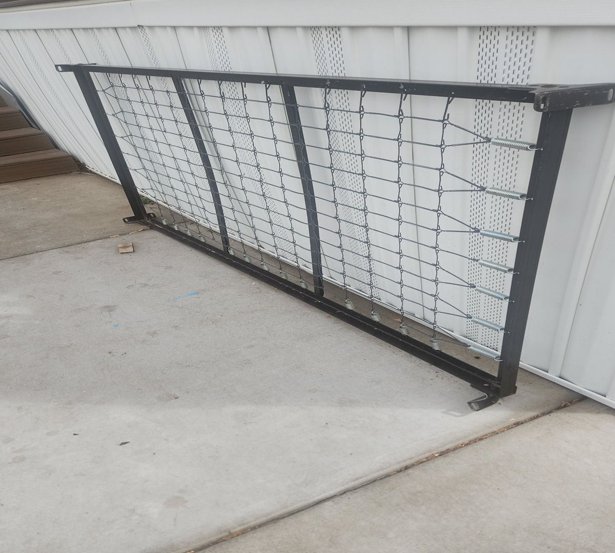 Black metal bed frame leaning against a white wall on a concrete patio.