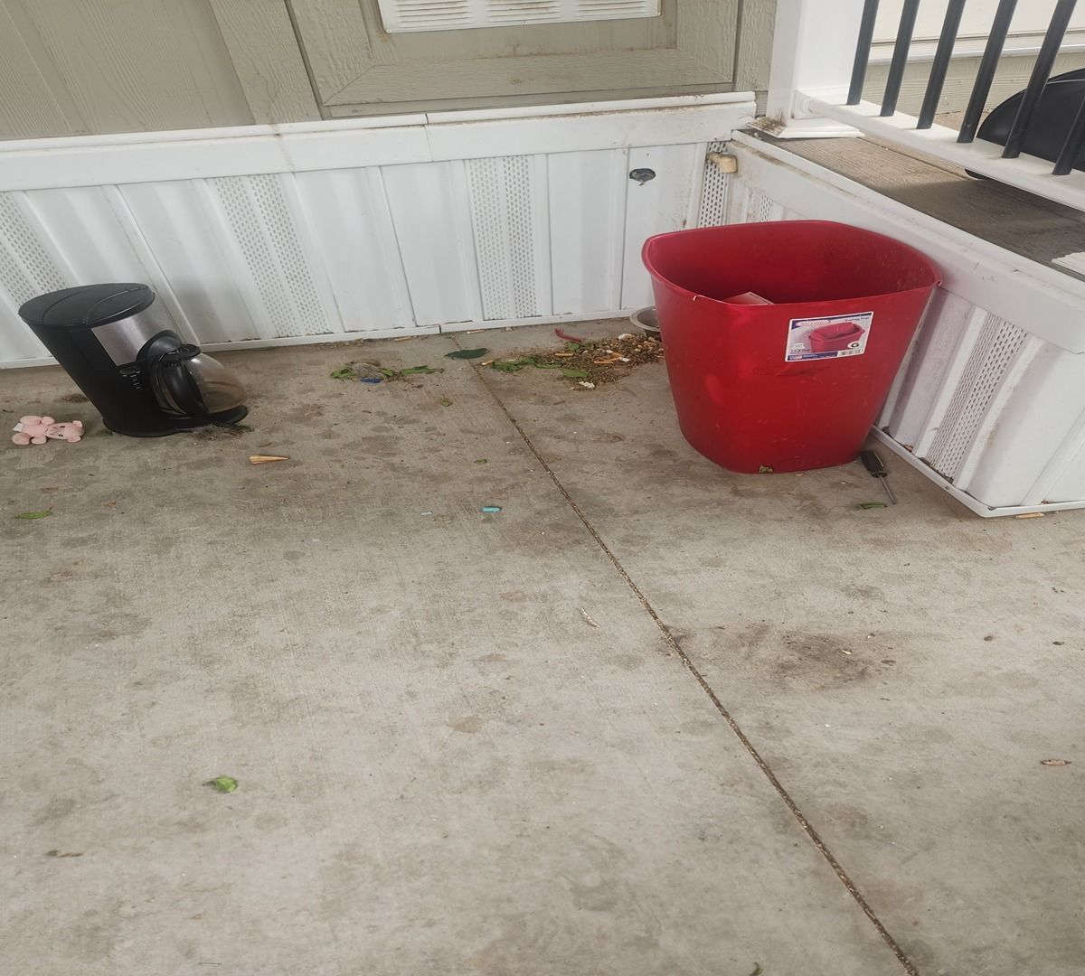 Concrete porch with a red bucket and black planter near a white railing.