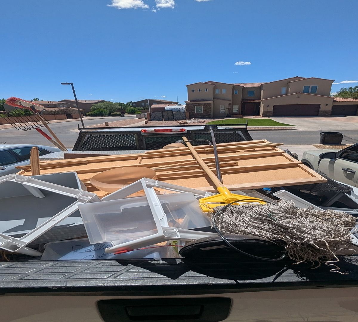 Truck bed piled with chairs, wood, and debris in a sunny residential street.
