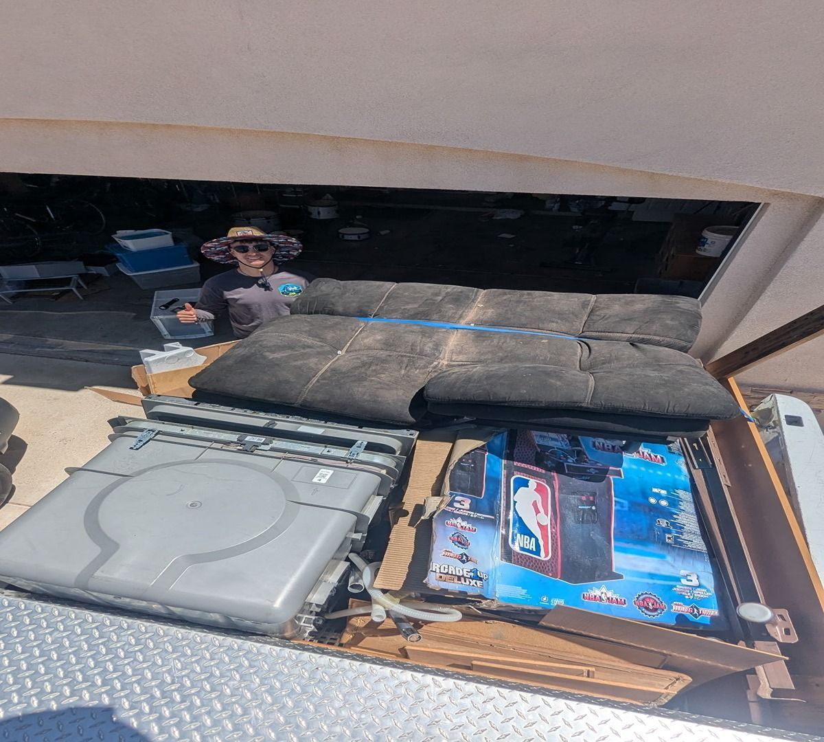 Opened truck bed with luggage, a gray hard case, and blue packaged items; person standing in background