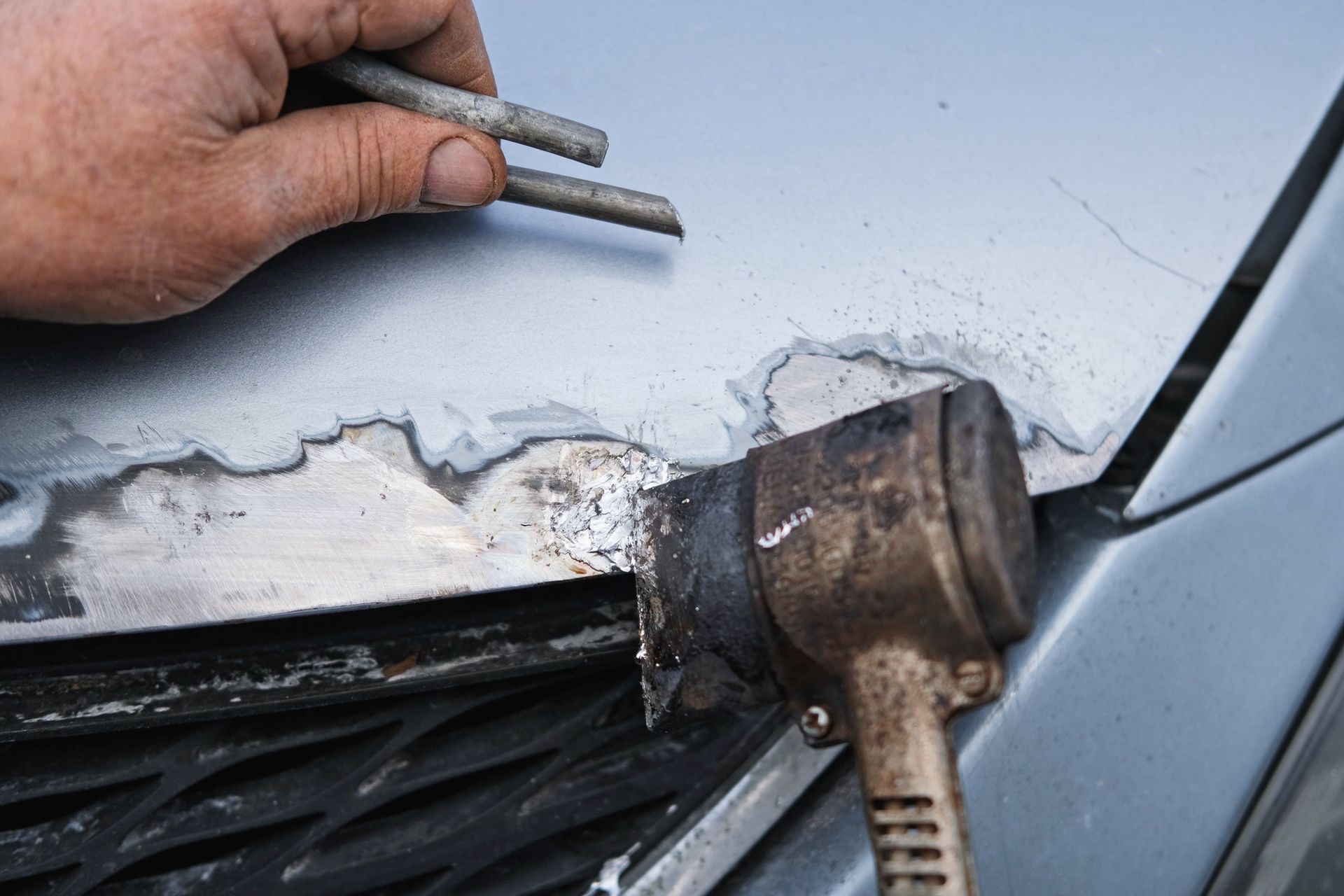 Welded metal joint being repaired on a car body with a hammer and chisel