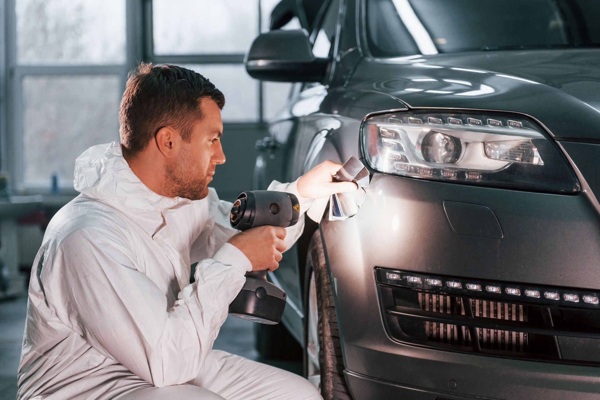 Mechanic inspecting a car’s front headlight with a power drill in a garage