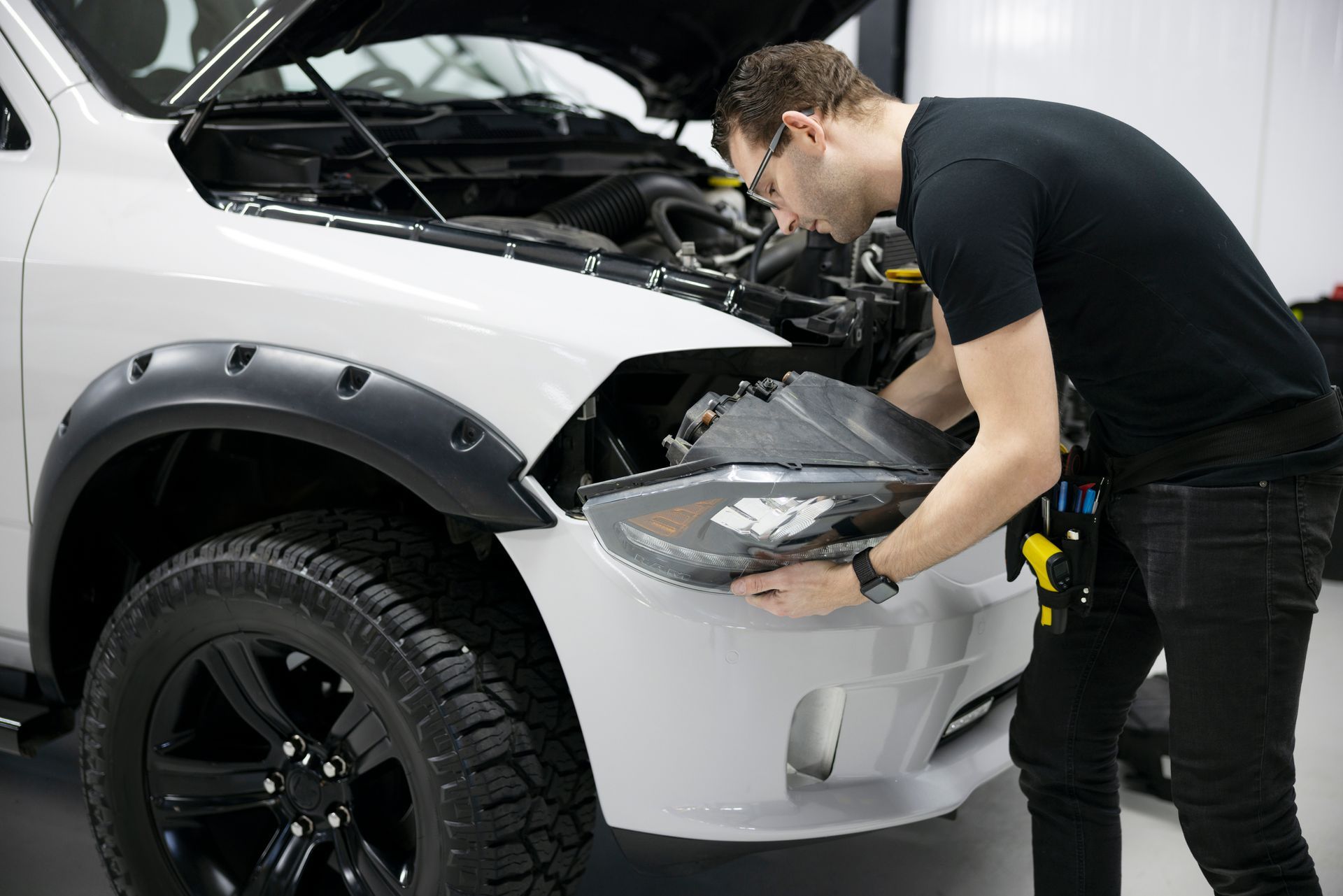 A man is looking under the hood of a white truck.