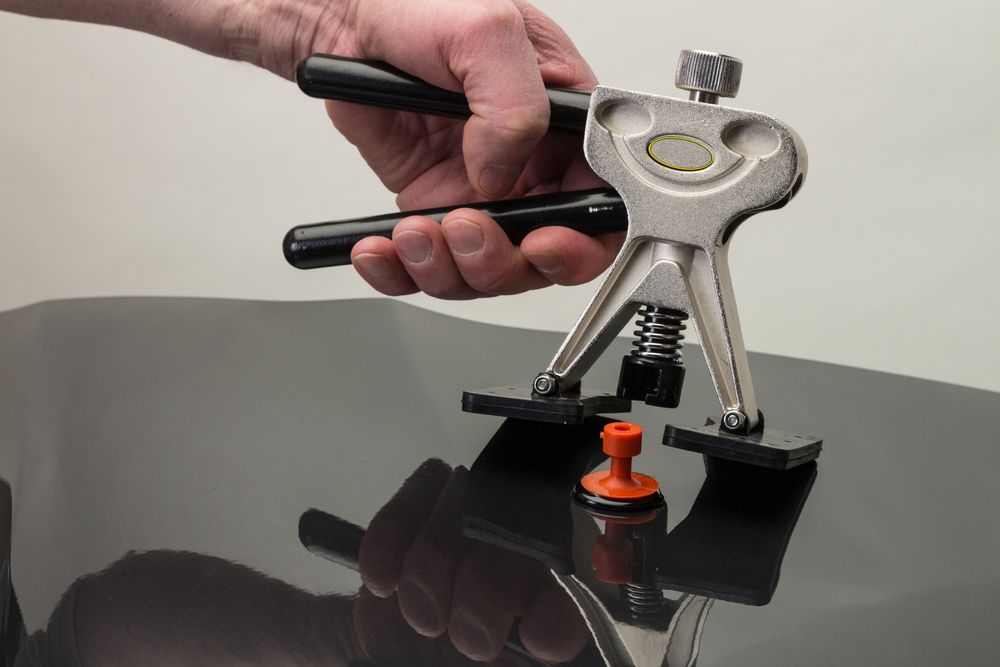 Hands operating a black-and-silver suction-cup tool on a glossy black surface, with an orange suction pad attached.