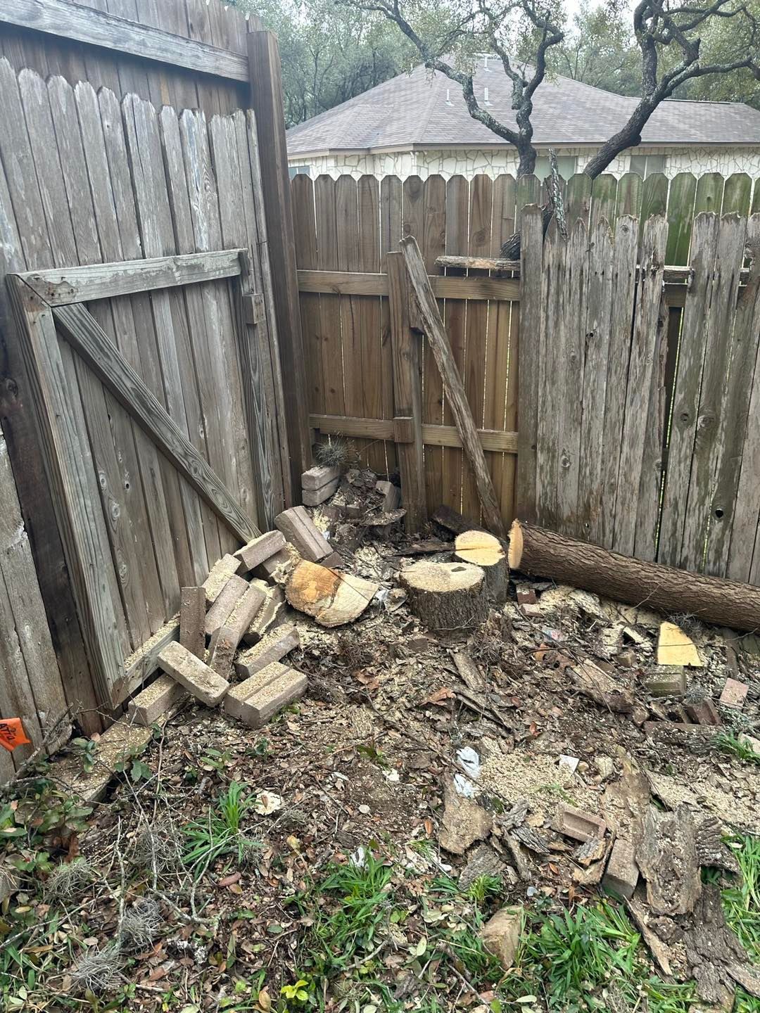 Wood debris near a fence. Cut logs, bricks, and a broken fence.