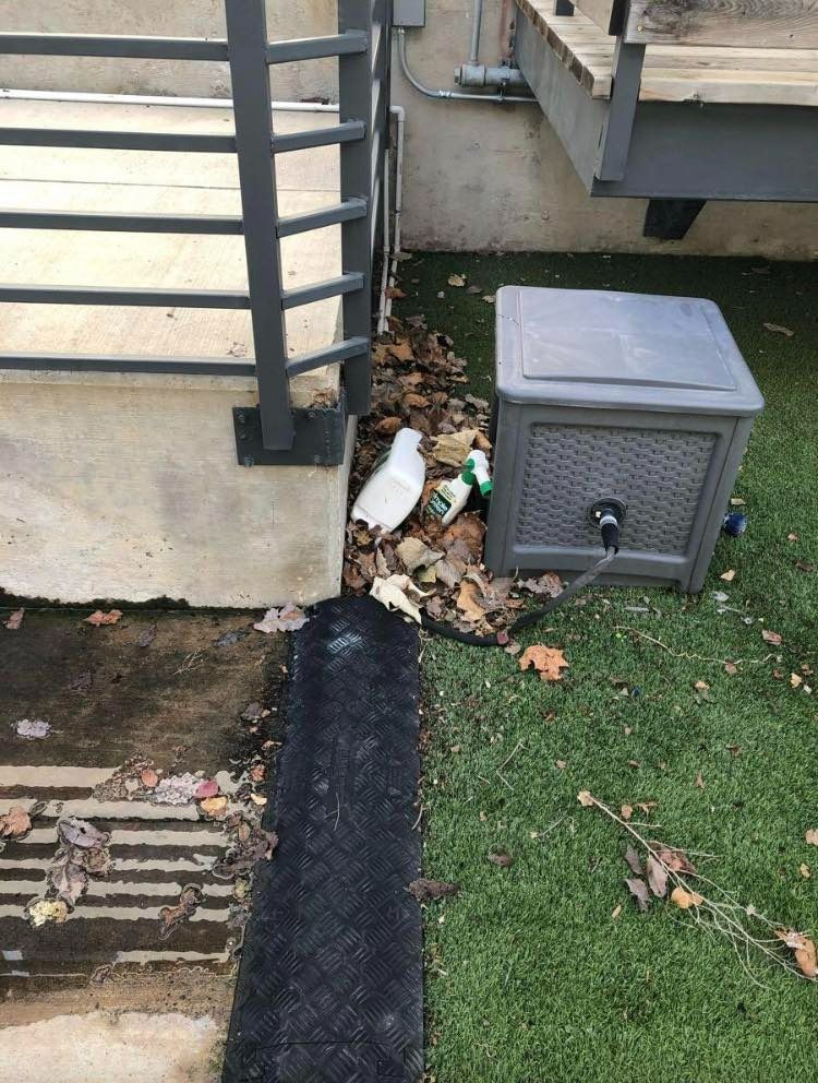 Debris, bottles, and a water cooler near a deck, on a section of artificial turf.