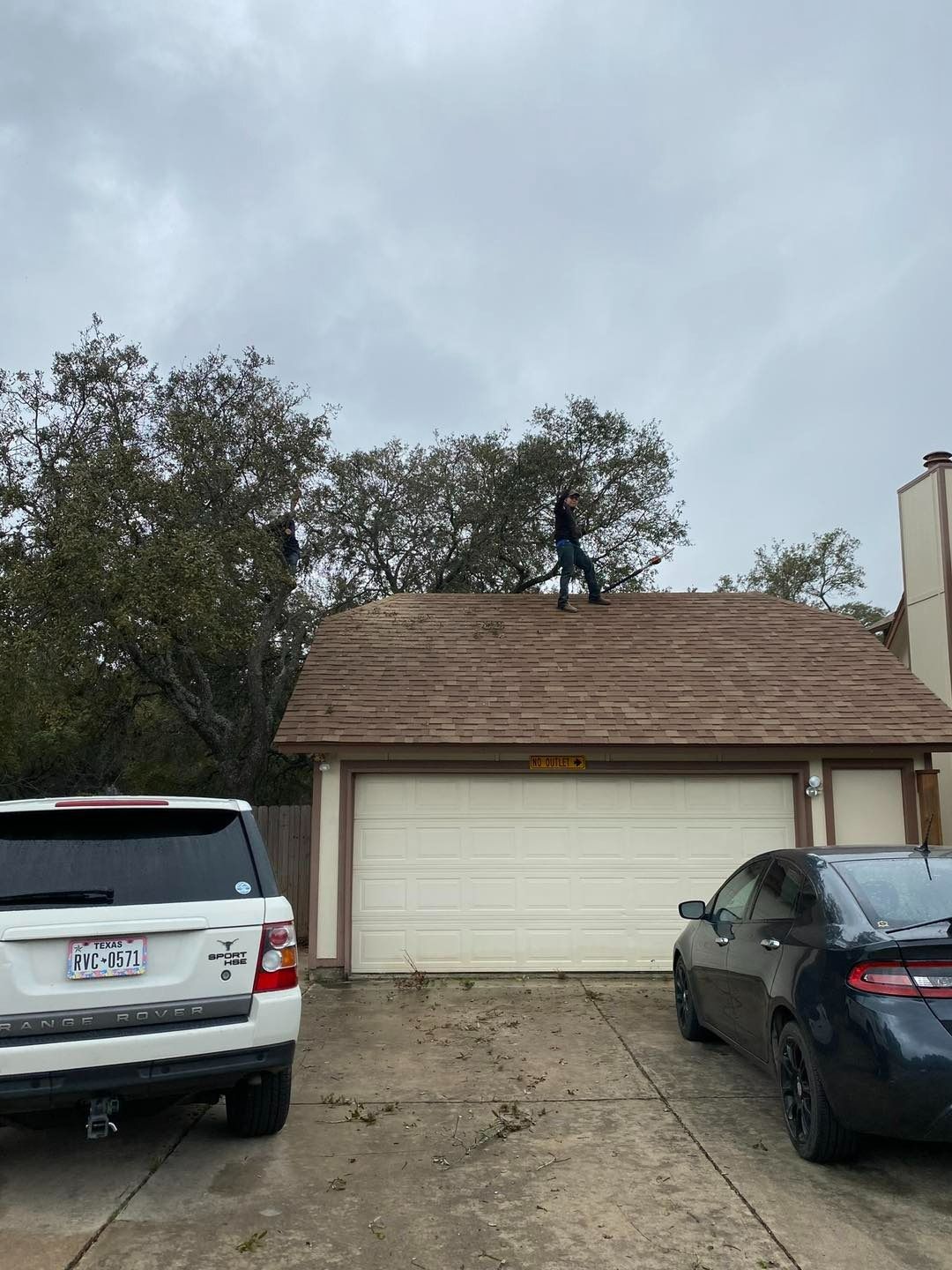 Person standing on a garage roof under a cloudy sky, with cars parked below.