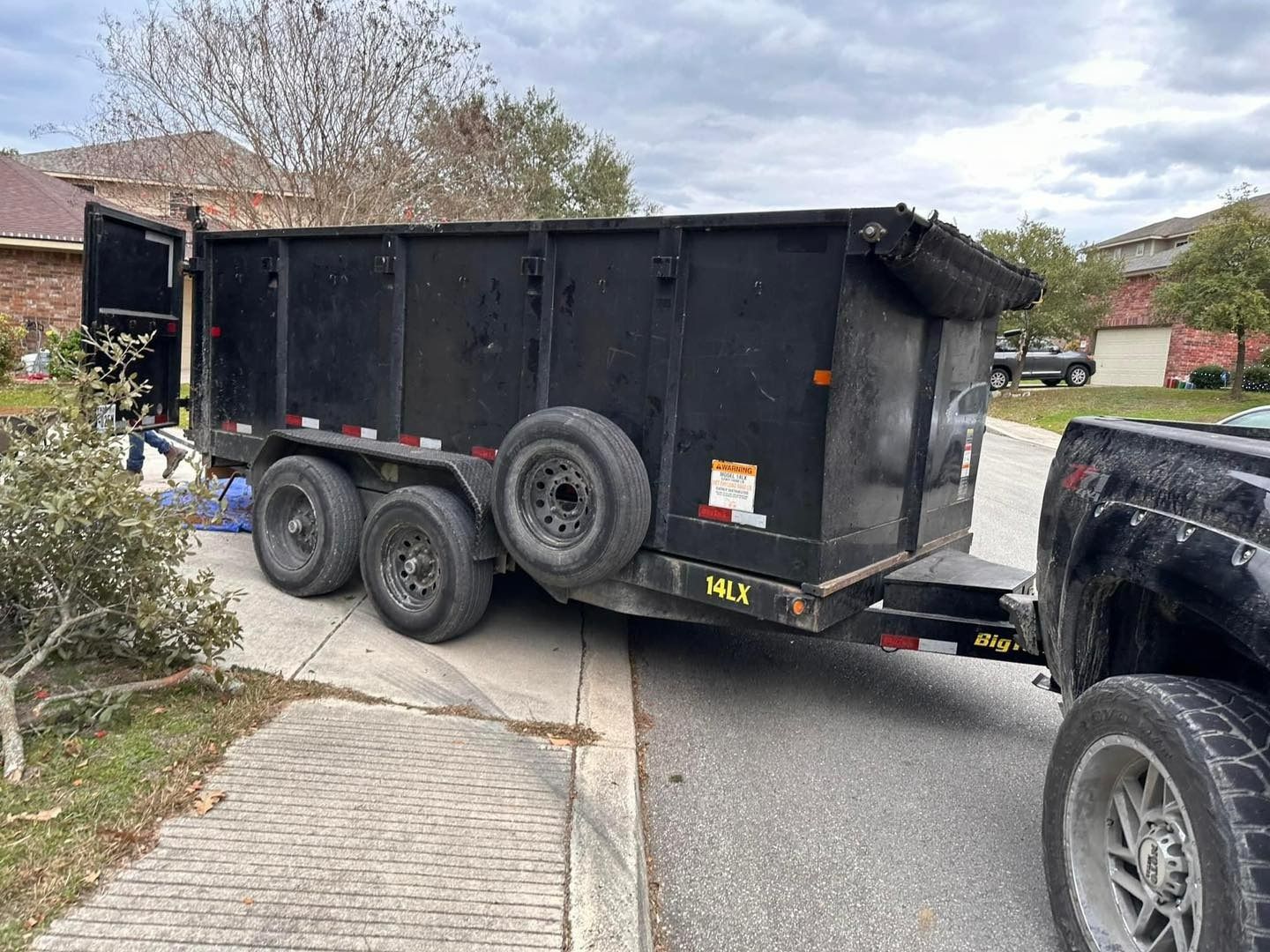Black dump trailer hitched to a truck parked on a residential driveway.