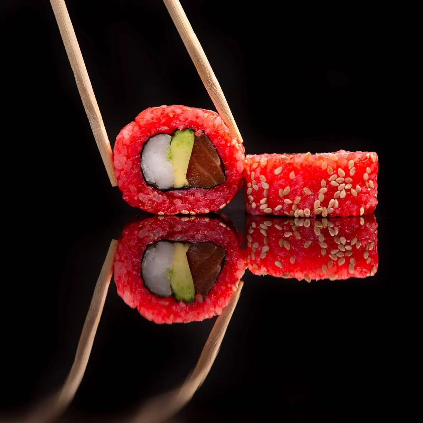 un par de palillos de madera sostiene un sushi rojo sobre una superficie negra
