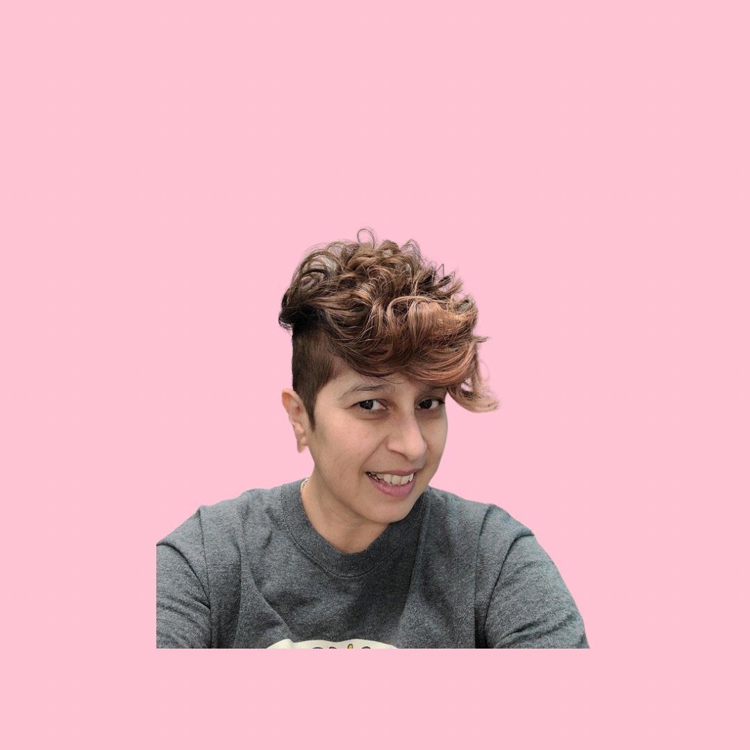 A woman with short curly hair is sitting in front of a pink background.