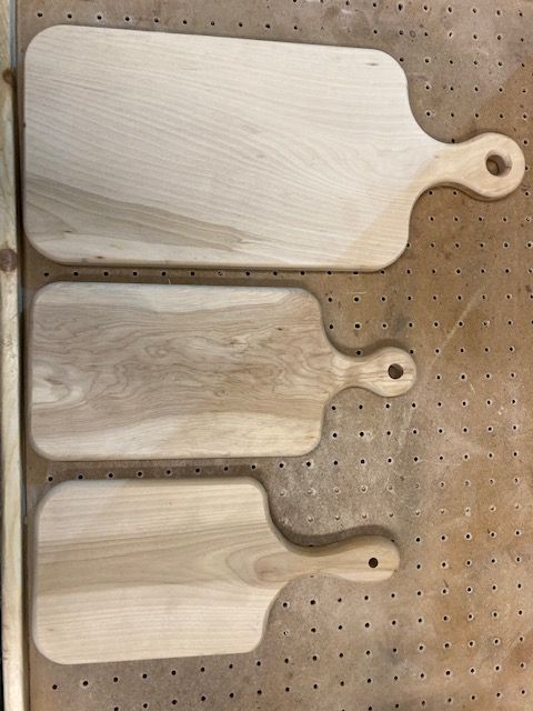 Three wooden cutting boards are sitting on a wooden table.