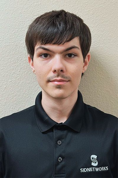 A man with dark hair and a thin mustache wearing a black polo shirt, standing in front of a neutral-colored wall.