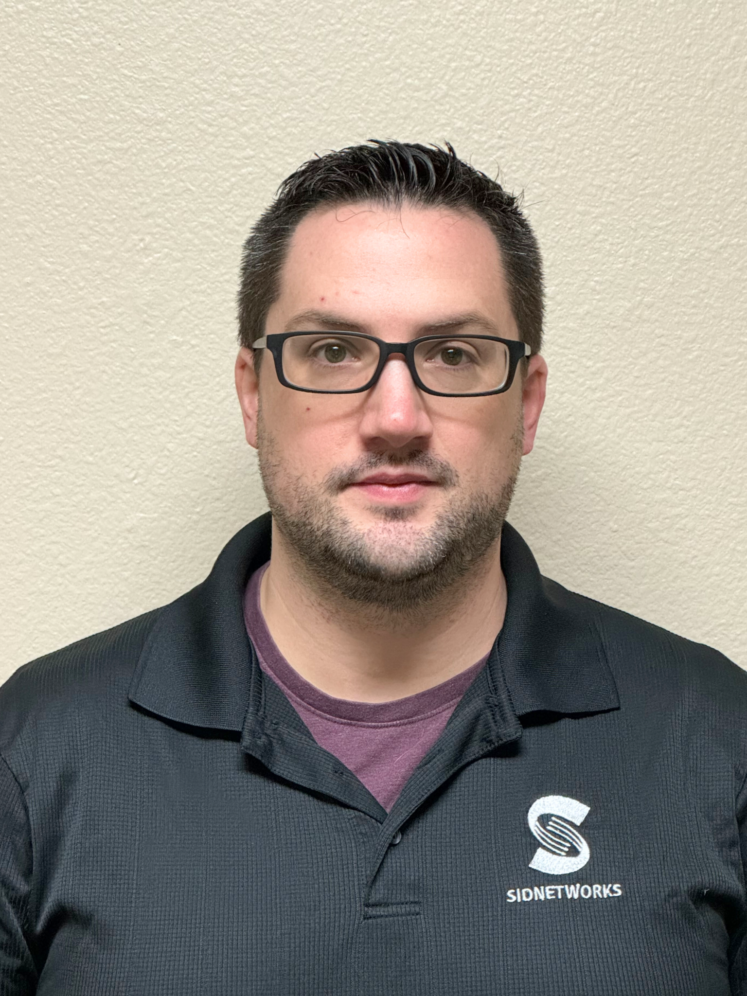 Man in black shirt with glasses, looking forward; logo on shirt.