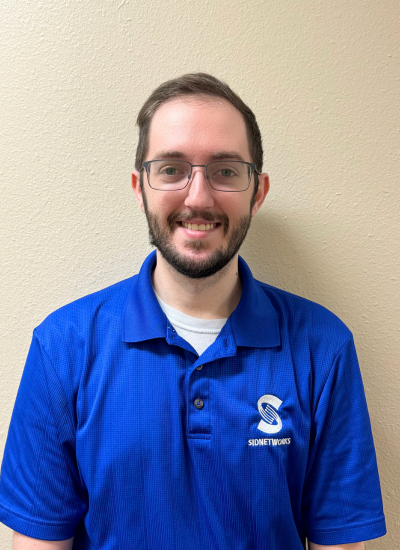 Man wearing glasses and a blue polo shirt smiling.