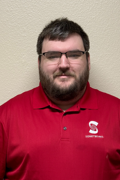 Man in a red polo shirt with glasses, a beard, and a logo over a light background.