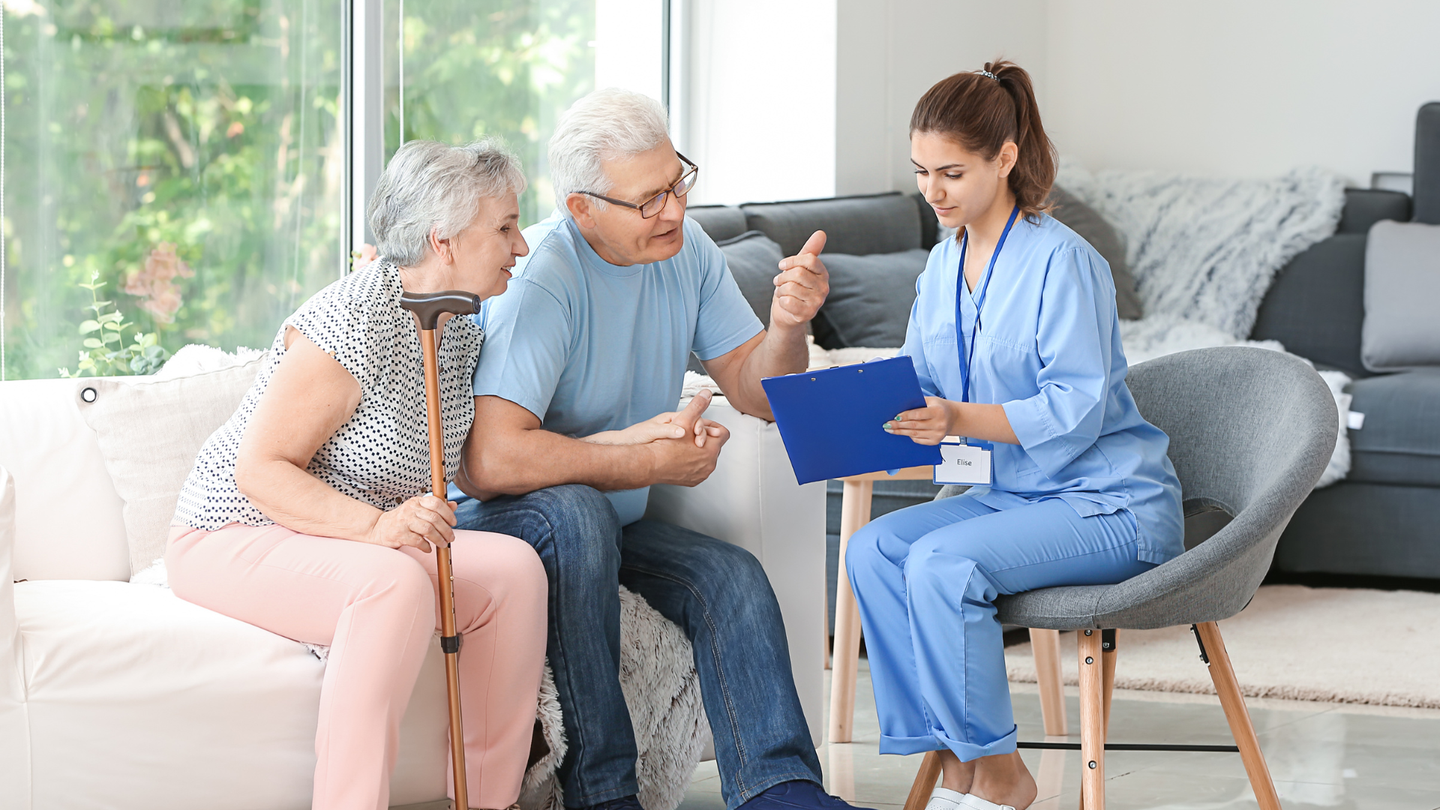 A nurse is talking to an elderly couple sitting on a couch.