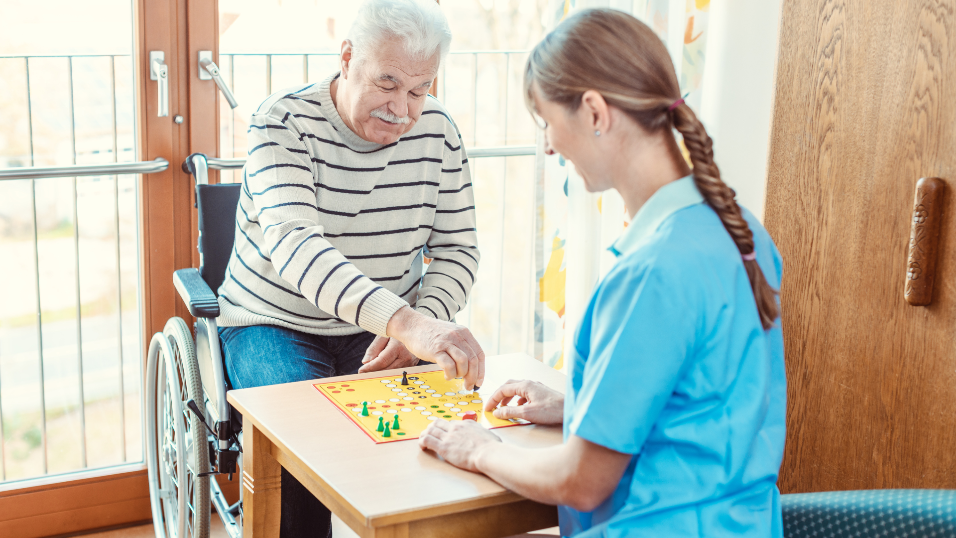 An elderly man in a wheelchair is playing a board game with a nurse.