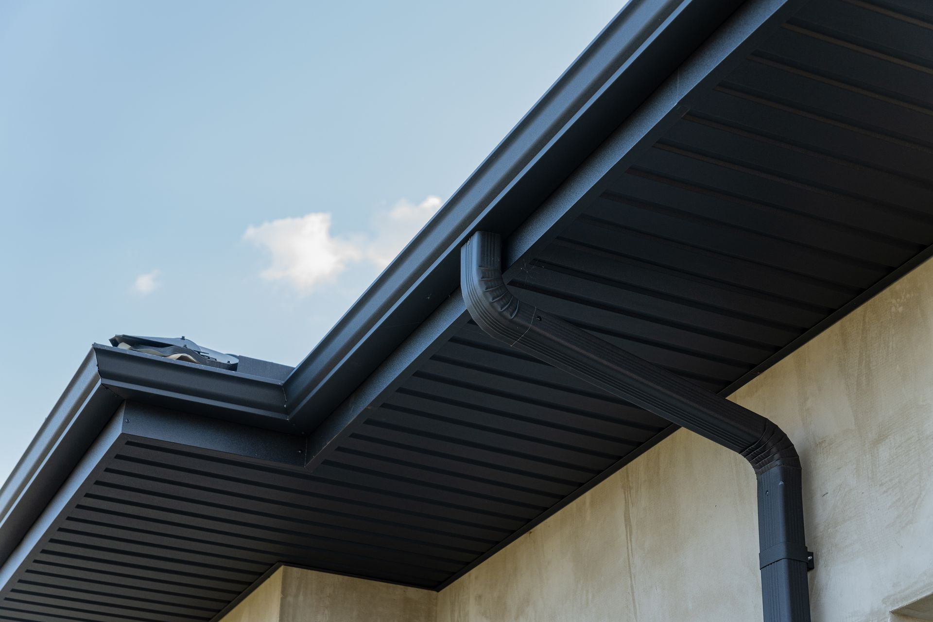 Black roof gutter and downspout on house exterior under blue sky.