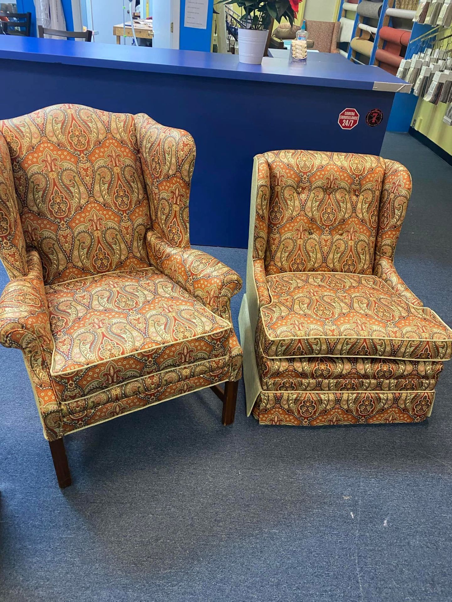 Two patterned upholstered armchairs, one larger and one smaller, displayed on a blue floor in a store.