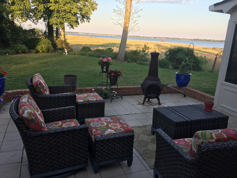 Patio seating overlooking a green lawn and distant water at sunset, with chairs, table, and chiminea