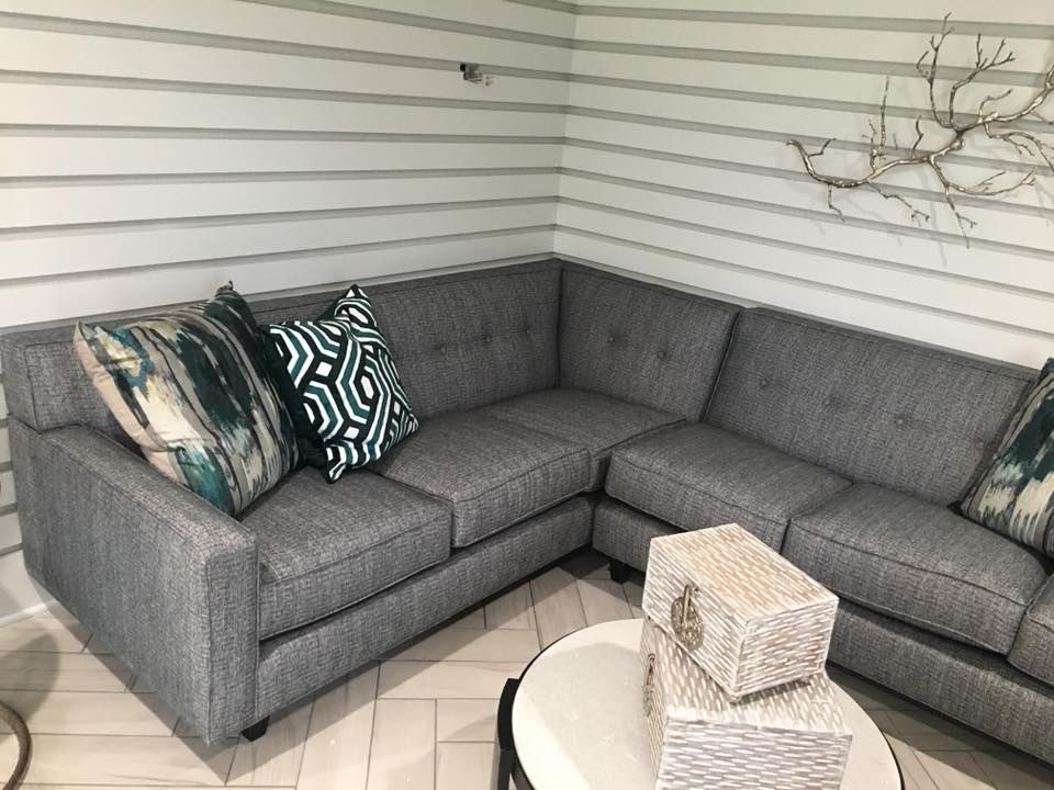 Gray sectional sofa with patterned pillows in a small covered porch, with a round white table and decor items.