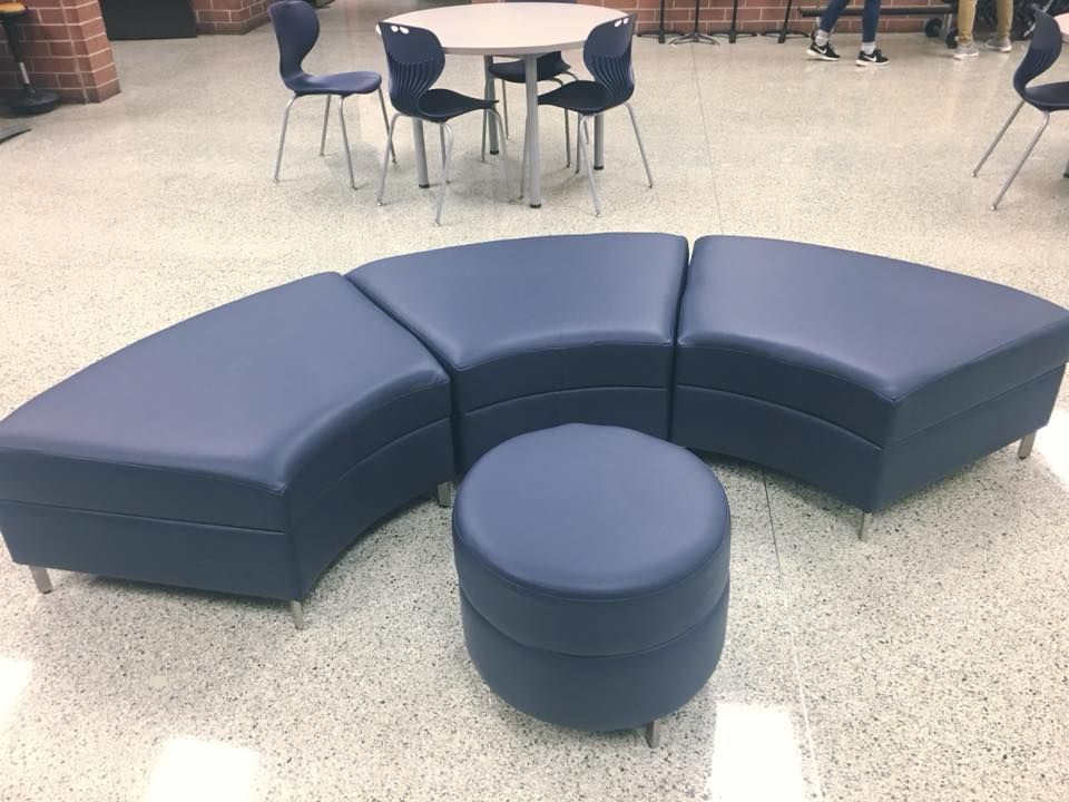 Curved blue modular seating with a round ottoman in a school cafeteria area