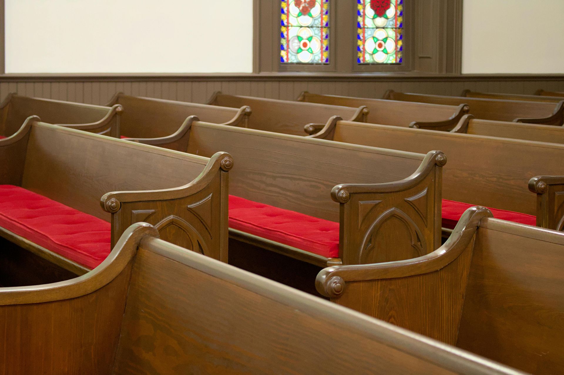 Empty wooden church pews with red cushions beneath stained glass windows