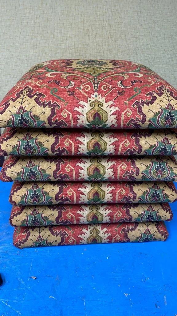 Stack of patterned folded cushions with floral red and gold design on a blue surface