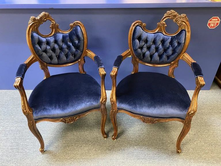 Pair of ornate blue velvet armchairs with gold carved frames on a light floor.