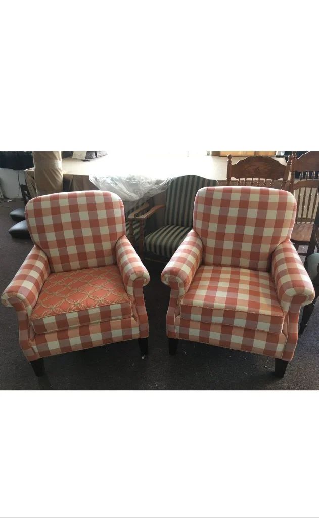 Two red-and-white checkered armchairs on a store floor, with a green striped chair behind them.