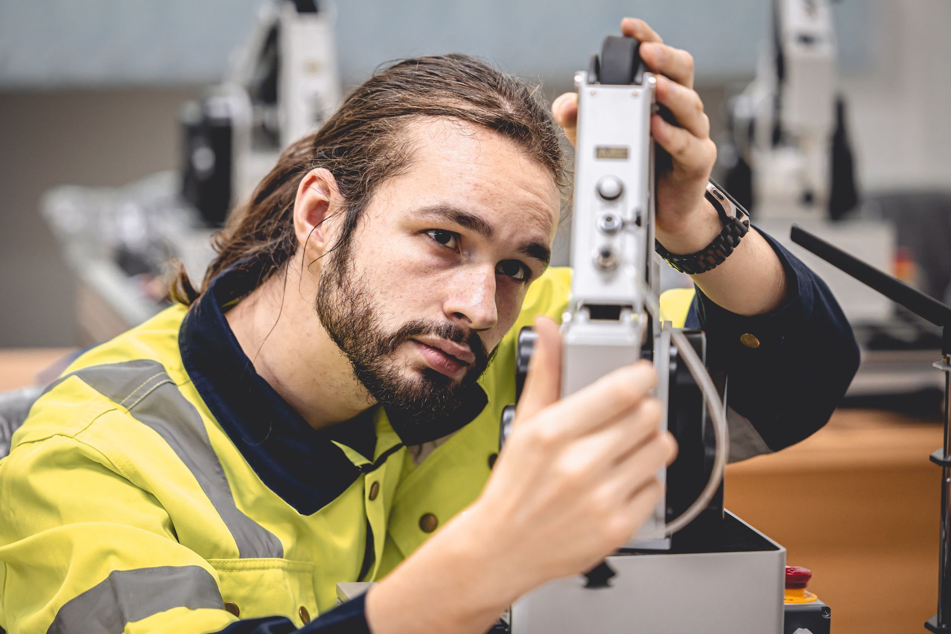 Ein Mann in einer gelben Sicherheitsweste arbeitet in einer Fabrik an einer Maschine.