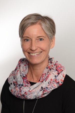 Eine Frau mit einem Schal um den Hals lächelt in die Kamera.