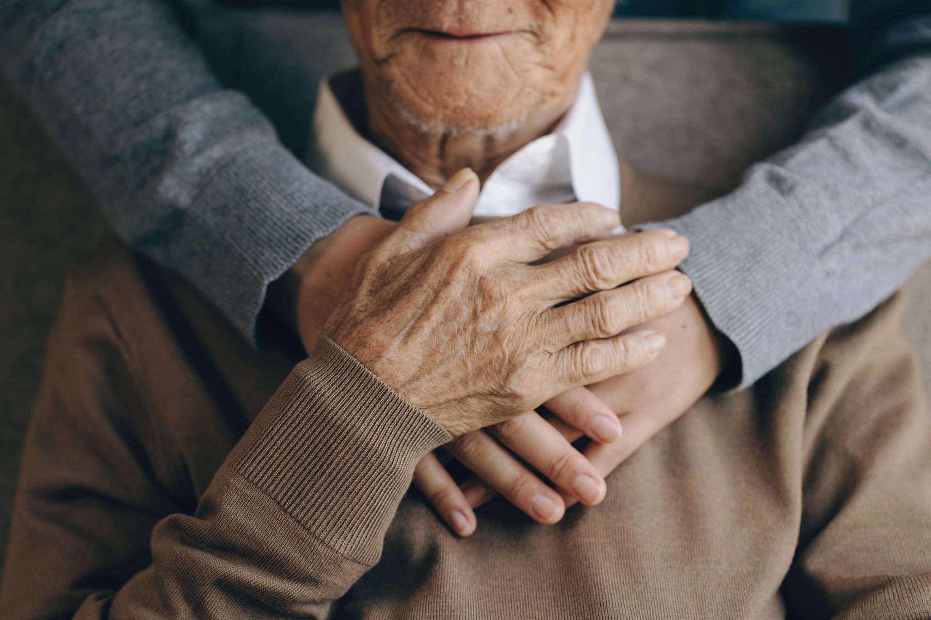 A close-up of a person with hands resting gently over the hands of another person, both wearing long-sleeved tops.