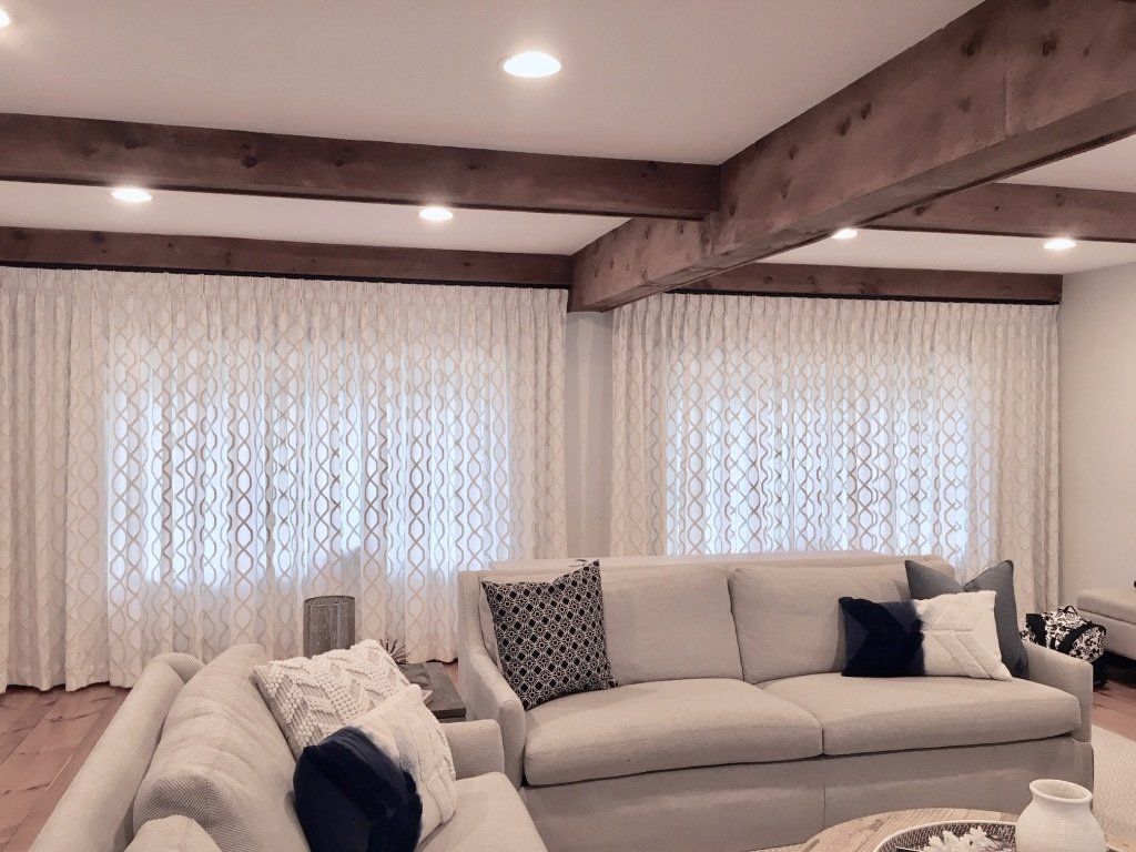 Living room with two cream-colored couches, patterned drapes, and wooden beams on the ceiling.