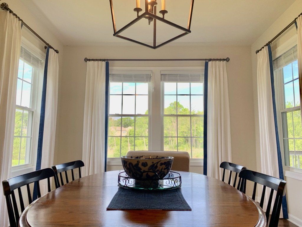Dining room with wood table and chairs, windows with white curtains and blue trim.