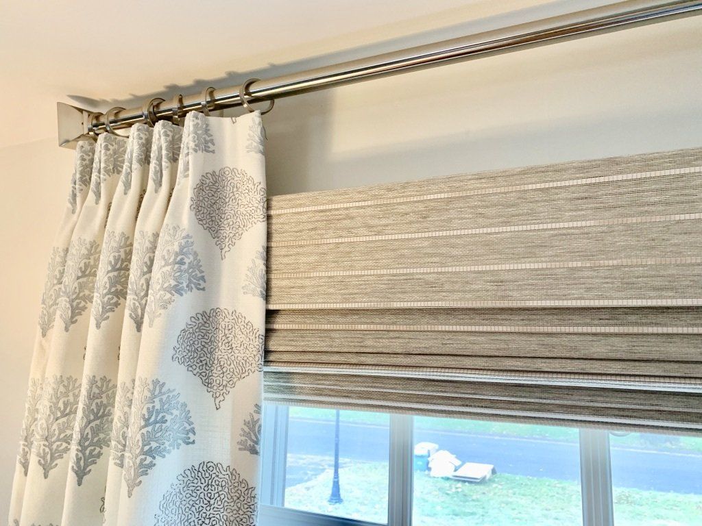 Drapery panel with leaf pattern and Roman shade over a window; silver curtain rod.