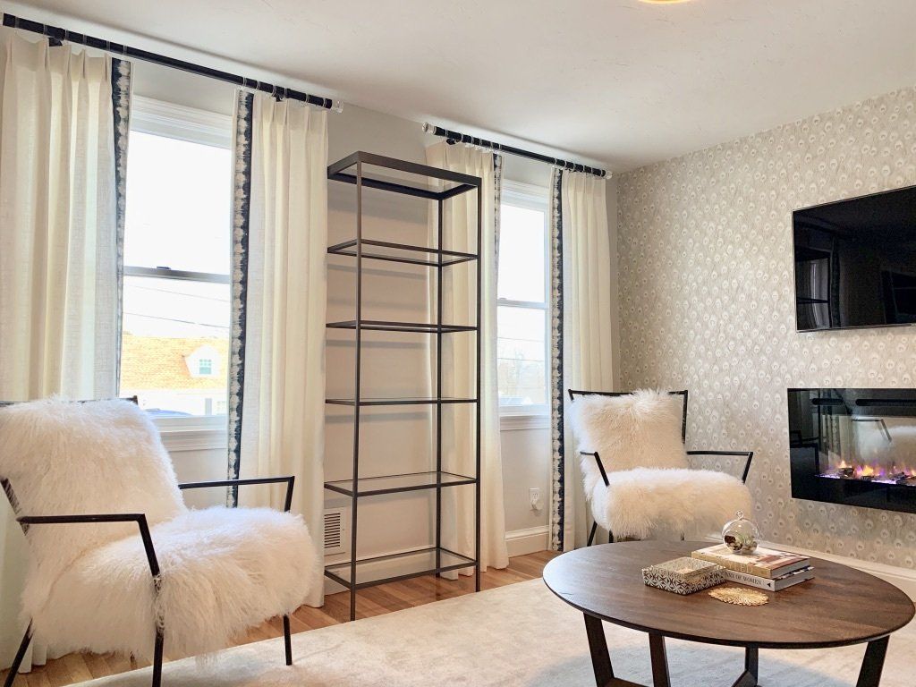 Living room with white fur chairs, round coffee table, fireplace, and tall black shelf.