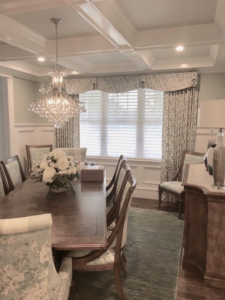 Elegant dining room with chandelier, long table, floral patterned curtains, and a coffered ceiling.