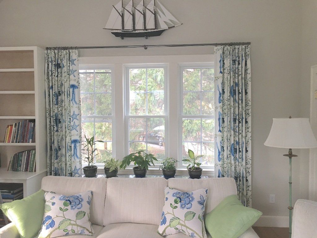 Living room with white sofa, blue and white patterned curtains, and sailboat decor above the windows.